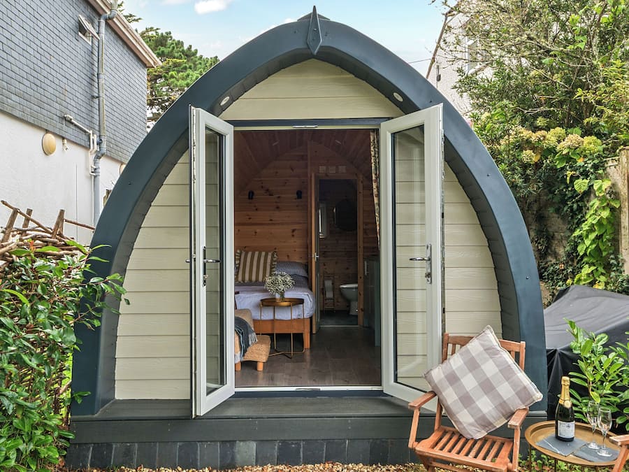 Una cabaña acogedora, semiabierta, con interior de madera, un pequeño comedor y vistas a un jardín.