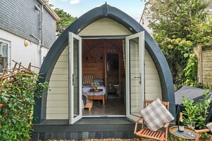 Una cabaña acogedora, semiabierta, con interior de madera, un pequeño comedor y vistas a un jardín.