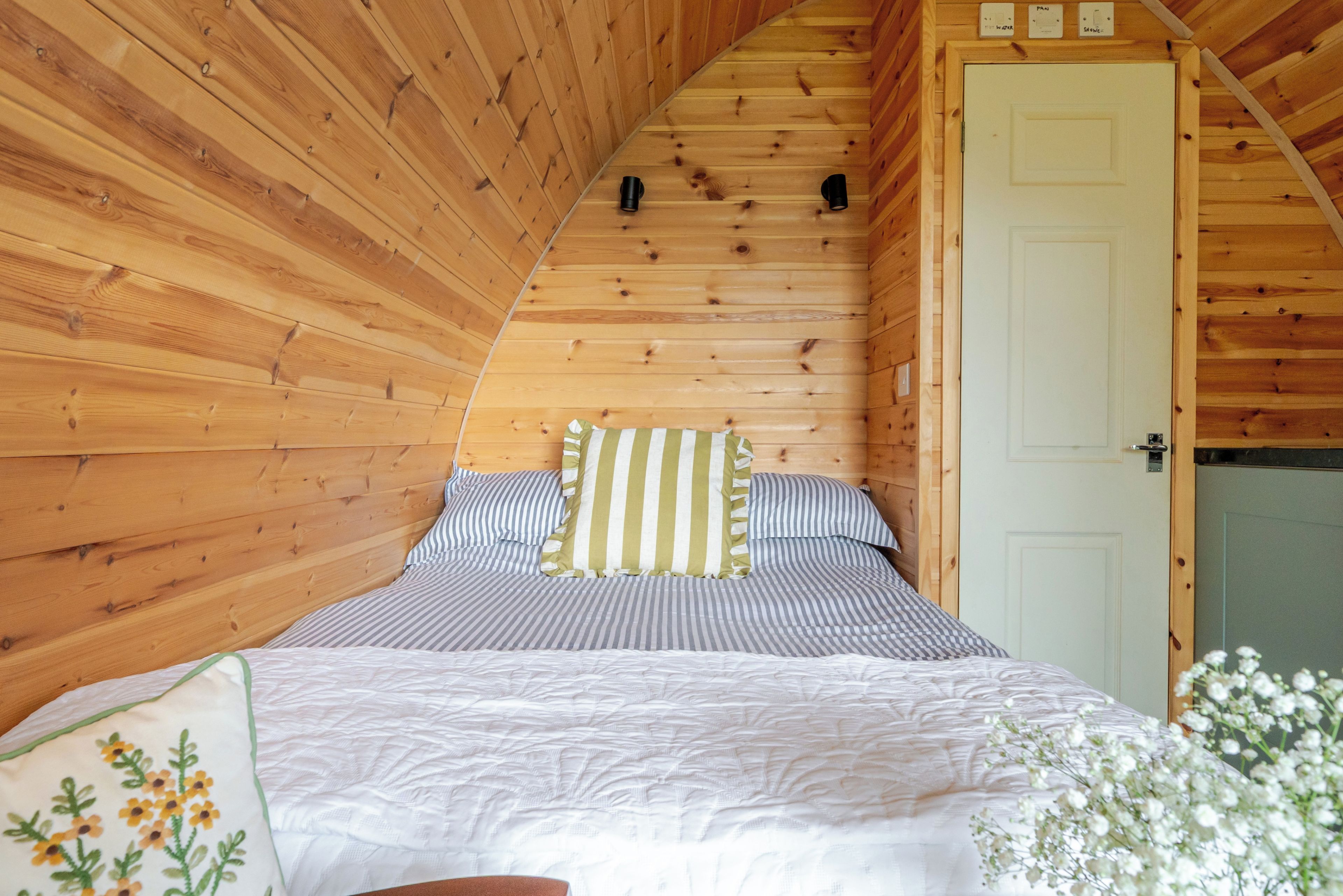 A wooden interior with a sloped ceiling, a bed with striped bedding, and a white door.