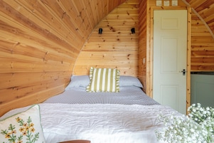 Un interior de madera con techo inclinado, una cama con ropa de cama a rayas y una puerta blanca.