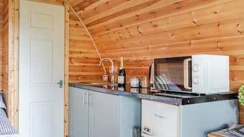 Cocina compacta con paredes de madera, una puerta blanca, un microondas, un lavamanos y un refrigerador pequeño.