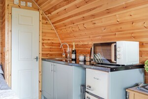 A compact kitchen with wooden walls, a white door, a microwave, a sink, and a small refrigerator.