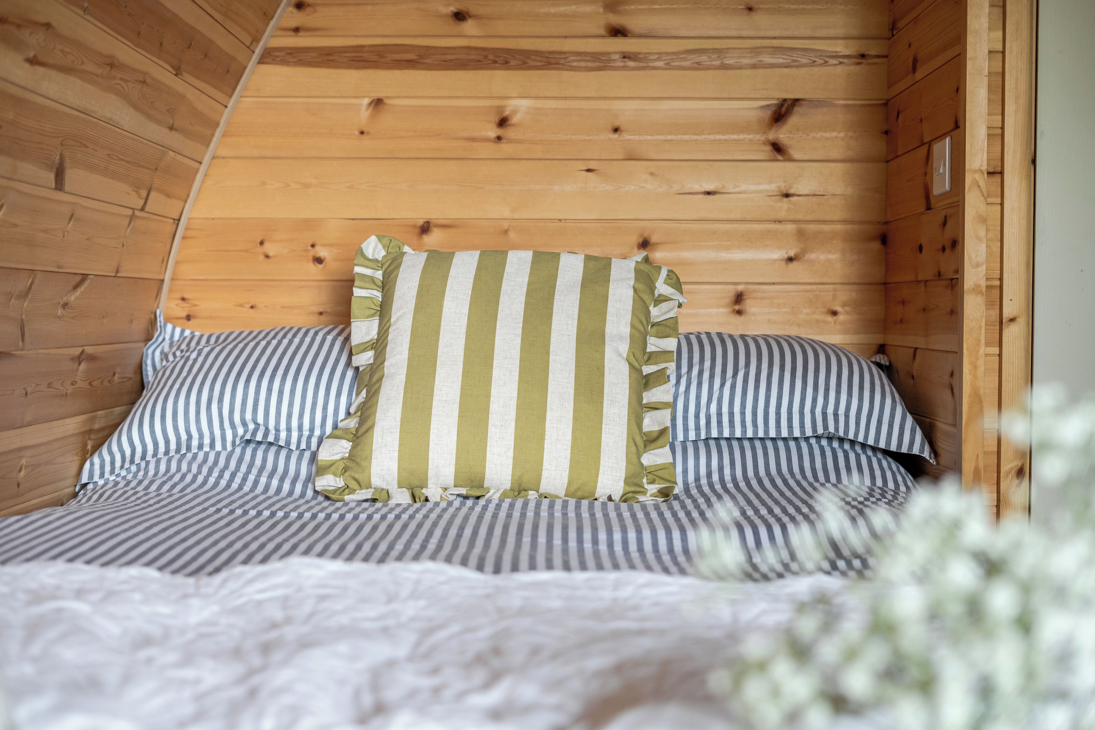 A wooden cabin interior with a bed featuring striped bedding and a pillow with vertical stripes.