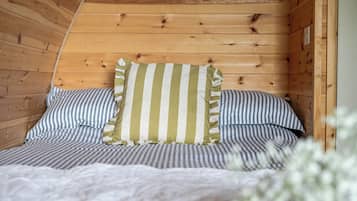 A wooden cabin interior with a bed featuring striped bedding and a pillow with vertical stripes.