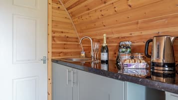 A kitchen with wooden walls, a stainless steel sink, a wine bottle, and a kettle.