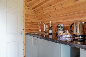 Una cocina con paredes de madera, un lavamanos de acero inoxidable, una botella de vino y un hervidor.
