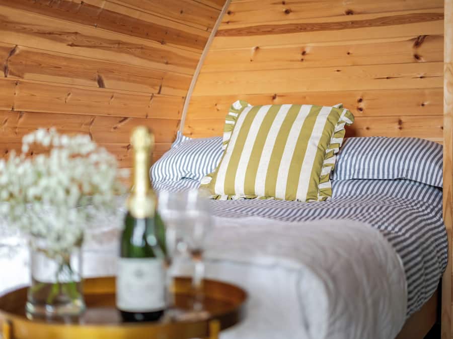 Una habitación de madera con una cama, almohadas y una botella sobre una mesa.