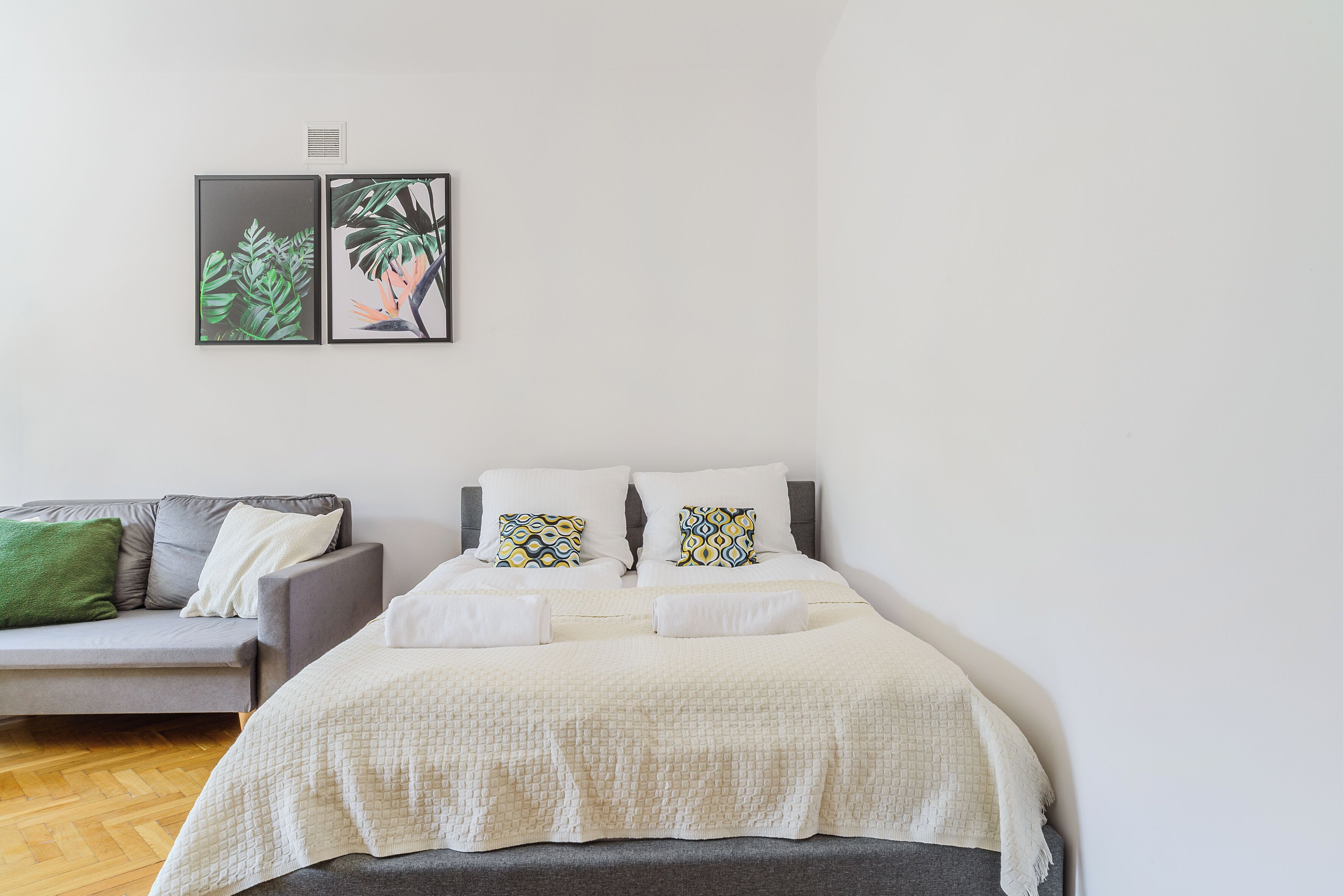 Um quarto com uma cama, um sofá cinzento e duas imagens emolduradas na parede.