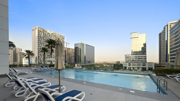A rooftop pool area with lounge chairs, a swimming pool, and high-rise buildings in the background. - Chic Studio Near Burj Khalifa, Dubai Opera & Dubai Mall w/ City Skyline Views (Dubai)