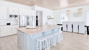 A modern kitchen with white cabinetry, stainless steel appliances, and a central island with bar stools. - Orange Beach House East Beach Front, Private Pool, Sleeps up to 28, Quiet Beach! (Orange Beach)