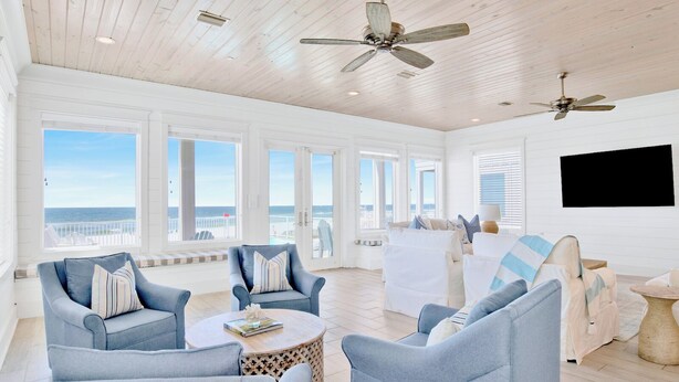 A spacious living room with a view of the ocean, featuring light blue furniture, ceiling fans, and a large window. - Orange Beach House East Beach Front, Private Pool, Sleeps up to 28, Quiet Beach! (Orange Beach)