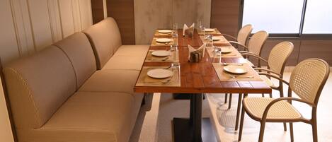 A dining area with a long wooden table set for six, surrounded by wicker chairs.