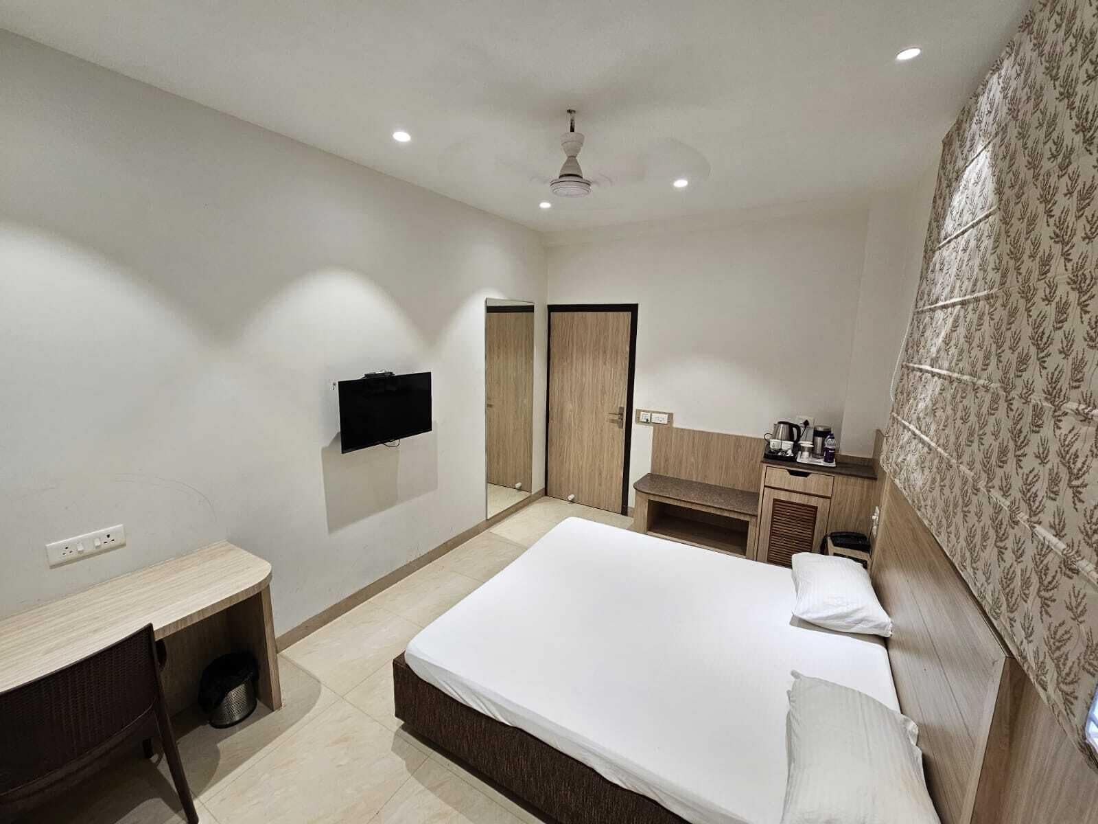 A modern hotel room with a large bed, a desk, a wardrobe, and a small kitchenette.