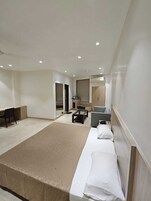 Quarto de hotel moderno com uma cama grande, uma escrivaninha, uma cadeira, uma mesinha e um sofá.