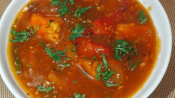 A bowl of soup with visible ingredients like tomatoes and herbs, placed on a textured mat.