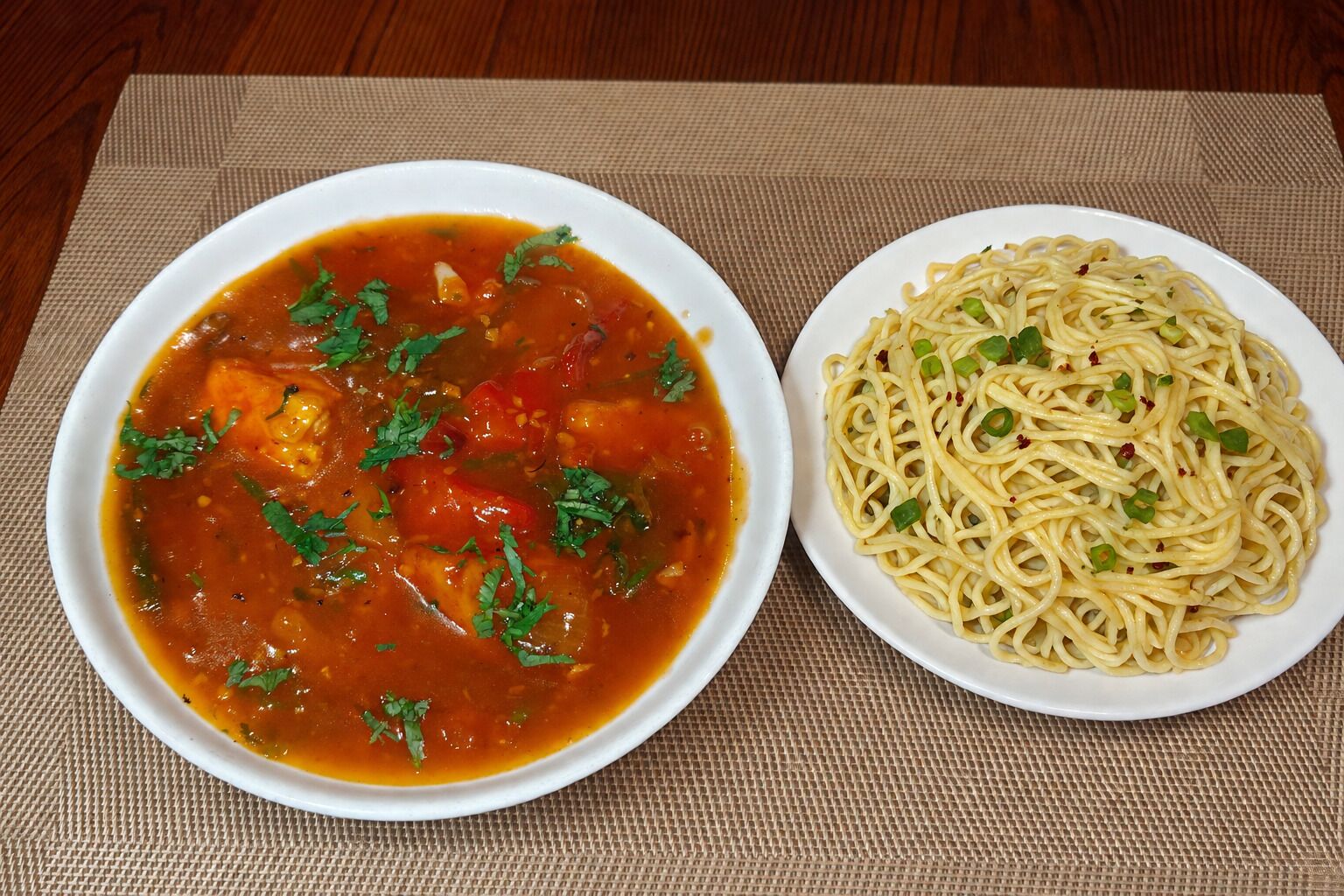 Two dishes, one appears to be a tomato-based soup and the other spaghetti, on a table with a woven placemat.