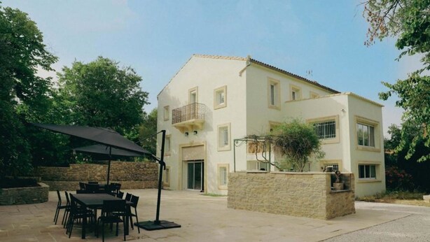 Un edificio de dos pisos con patio, mobiliario exterior y una pared de piedra.