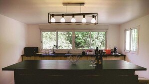 Una cocina con una isla grande, un ventanal con vistas a árboles y una lámpara moderna sobre la isla.