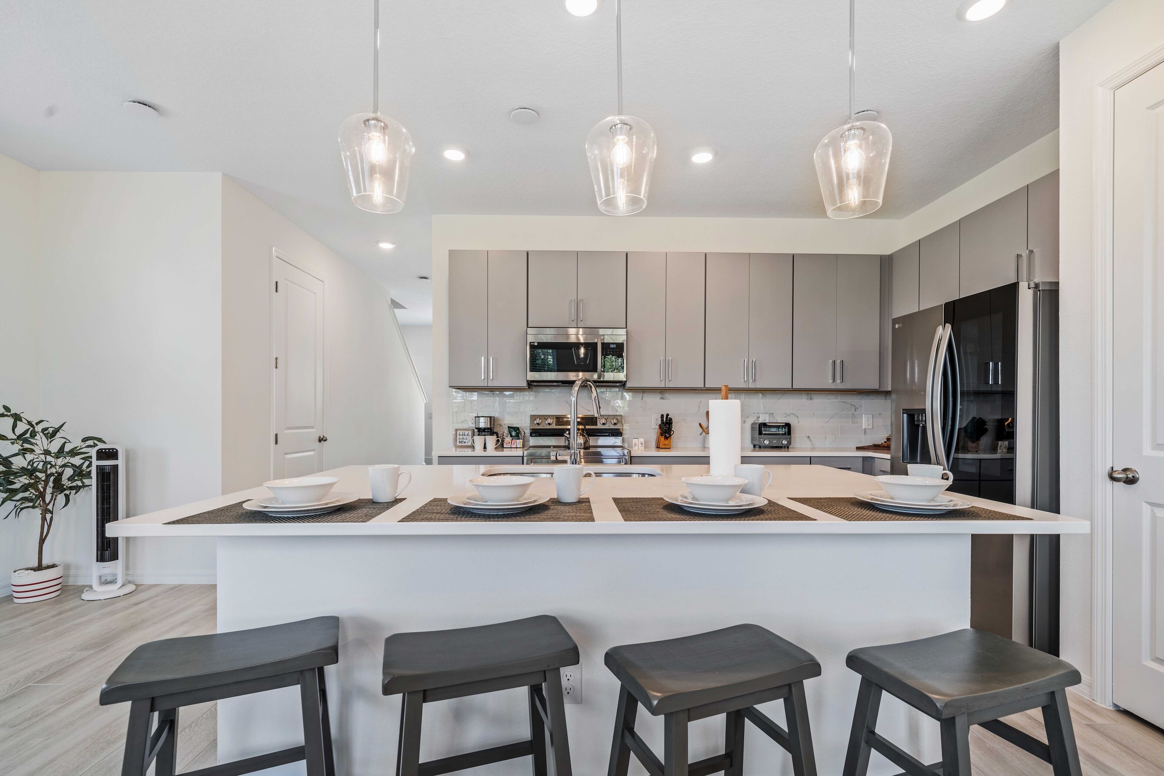 A modern kitchen with a central island, bar stools, pendant lighting, and stainless steel appliances.
