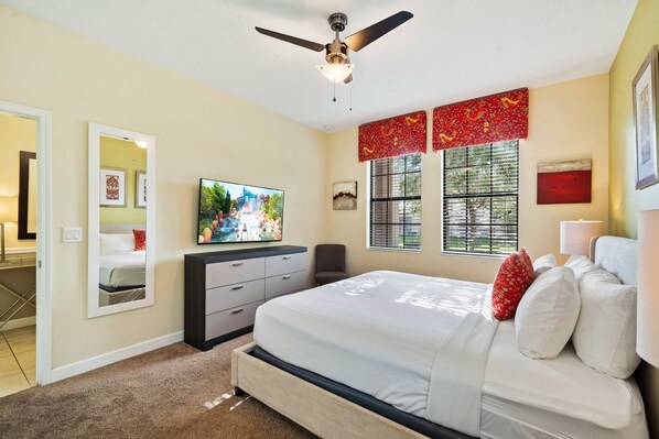A bedroom with a bed, a ceiling fan, a TV, a window with blinds, and a door leading to a bathroom. - 1467 Rolling Fairway Drive (Davenport)