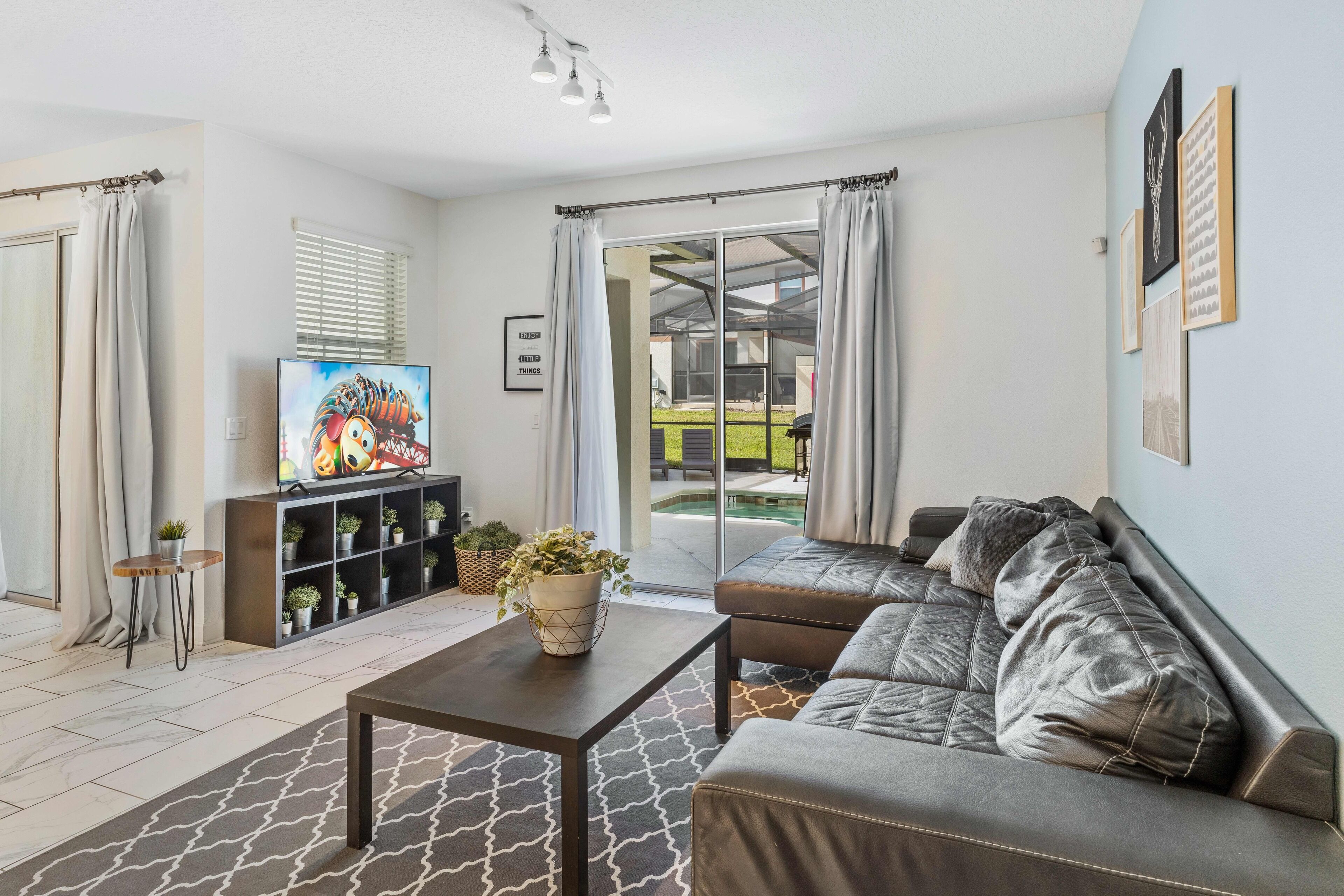 A modern living room with a sofa, a coffee table, and a TV. There is a sliding glass door leading to an outdoor area.