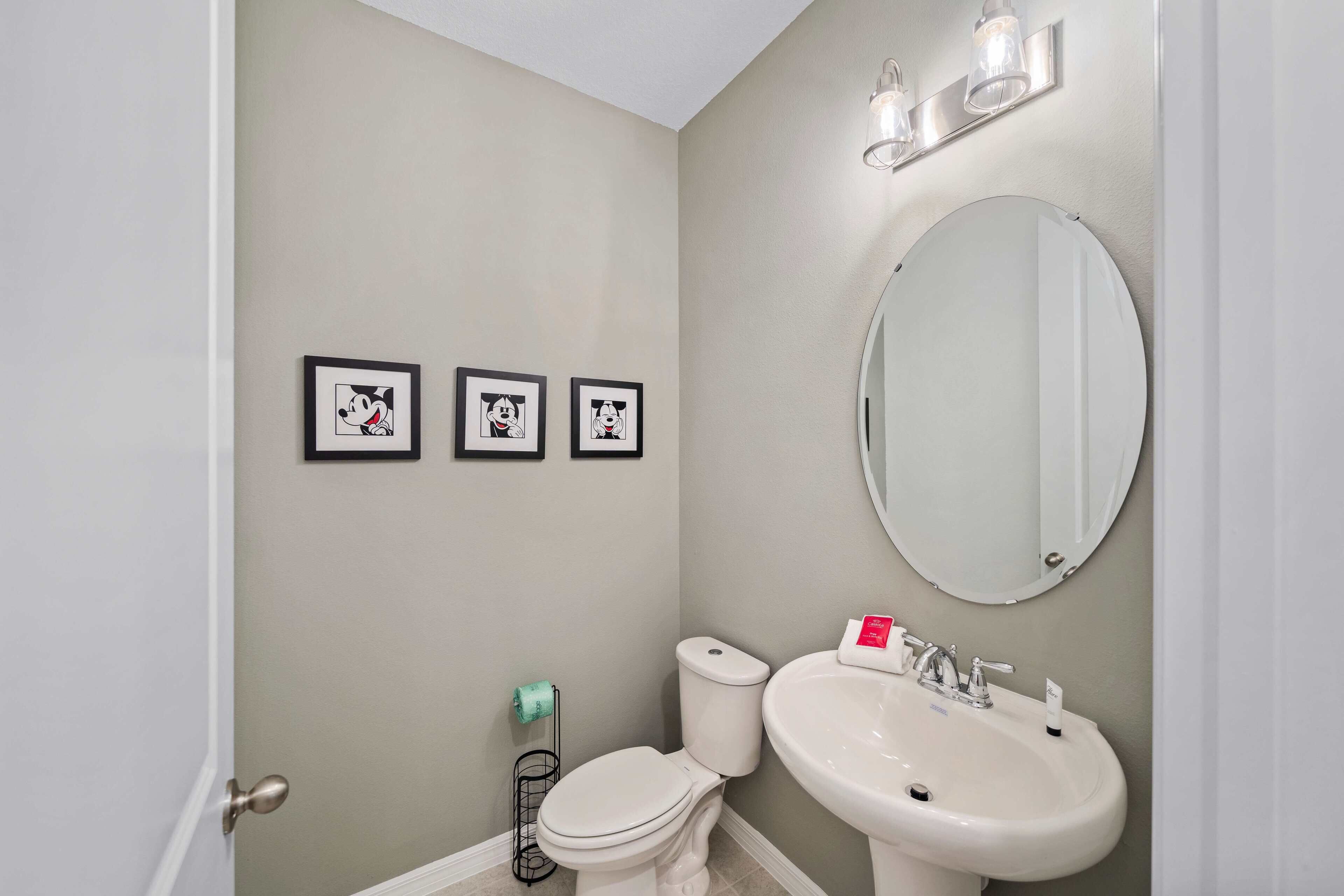 A bathroom with a toilet, sink, and three framed pictures on the wall.