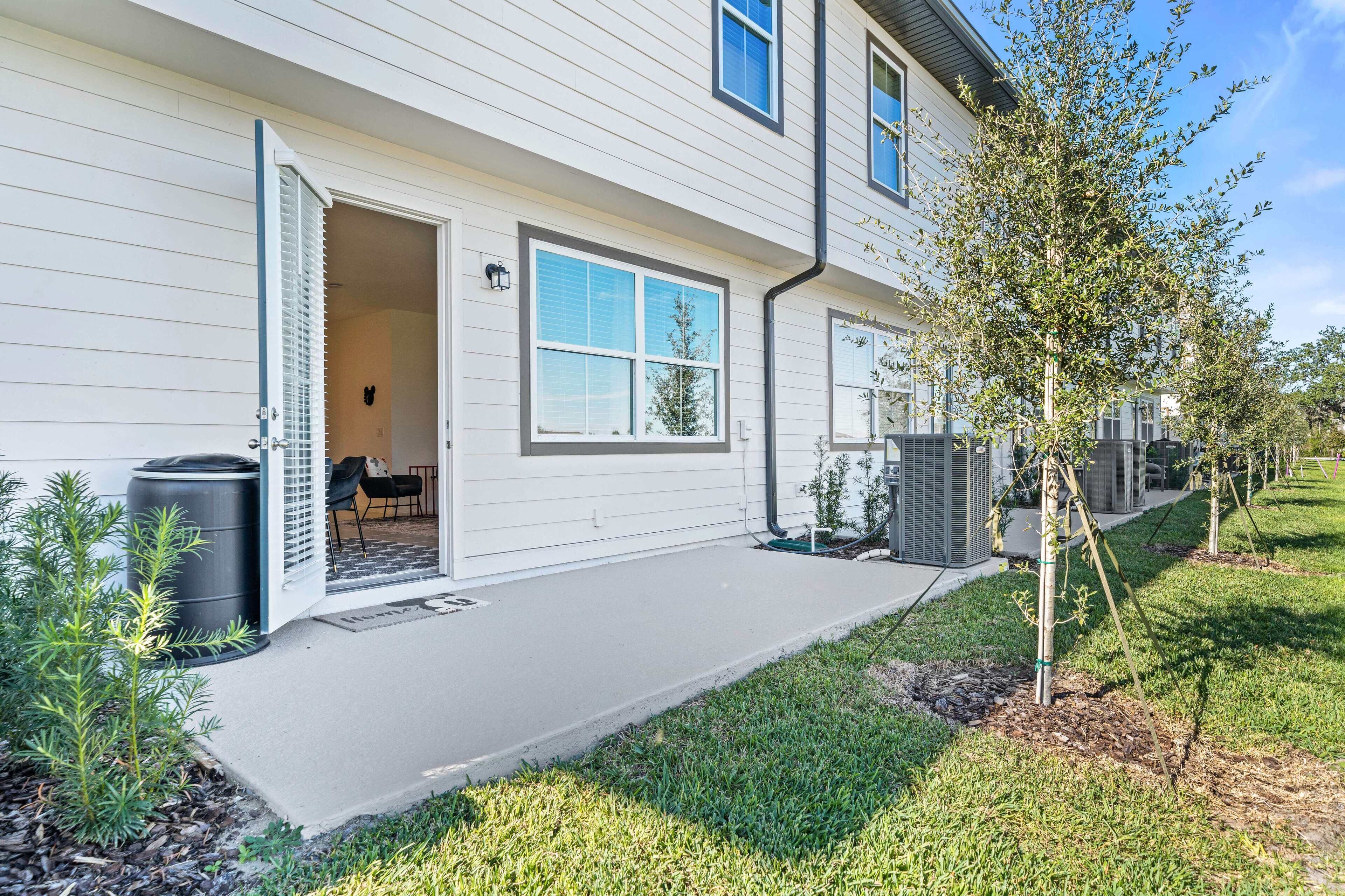 A modern two-story house with a covered patio, a small garden, and a visible outdoor seating area.