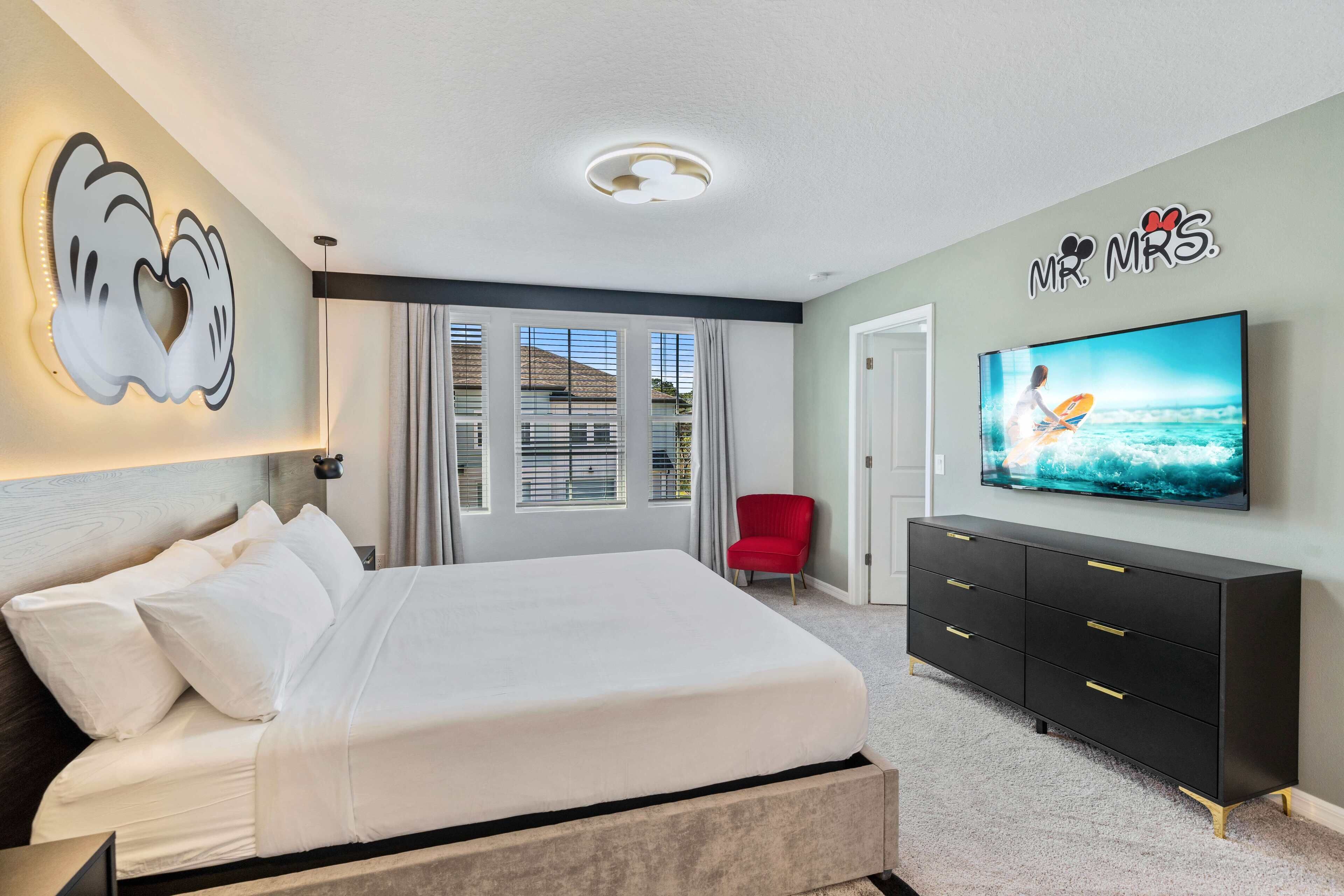 A bedroom with a bed, a TV, a red chair, and a wall with a heart-shaped design.