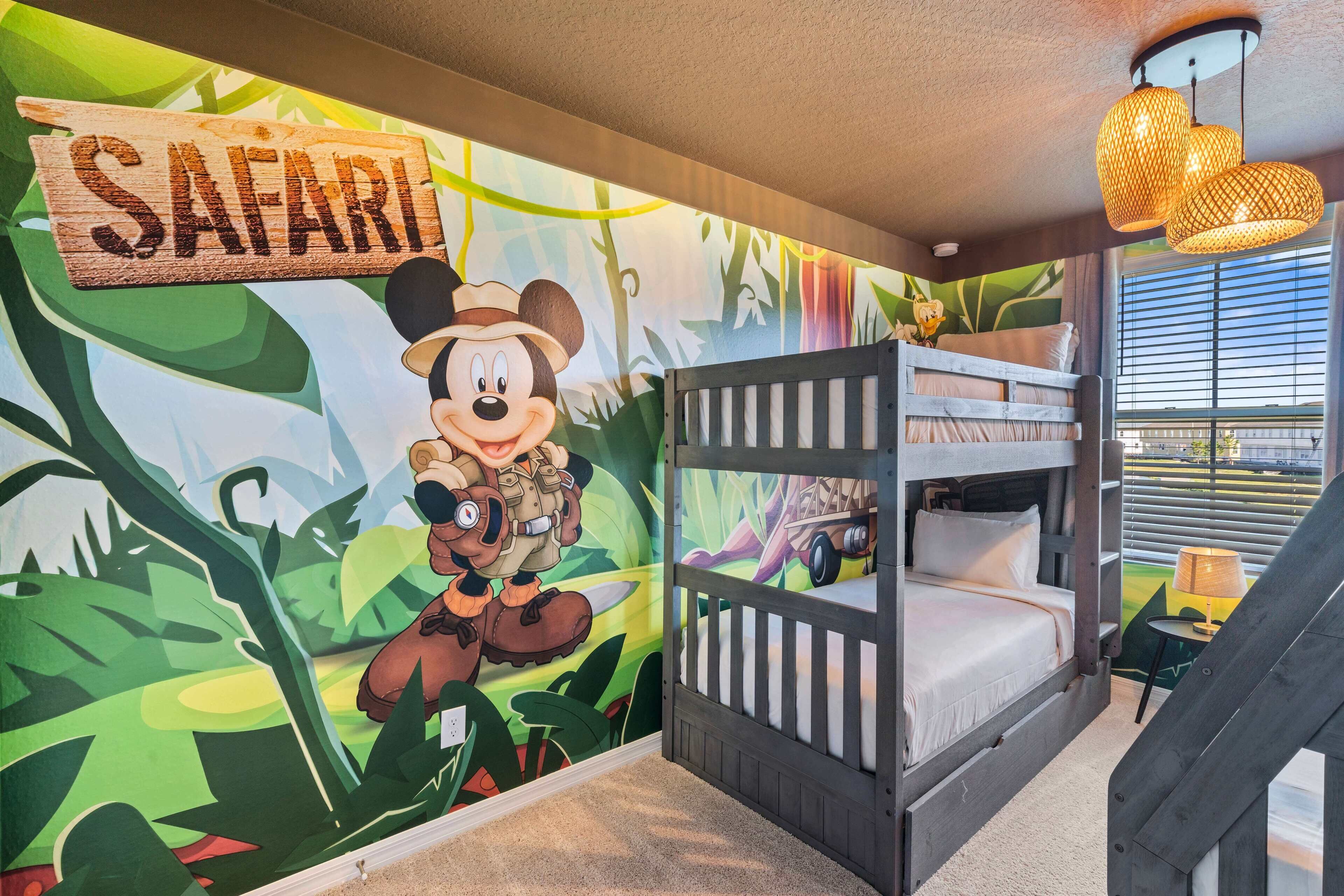 Une chambre d’enfant avec une fresque murale représentant Mickey Mouse, un lit superposé et une enseigne « Safari ».