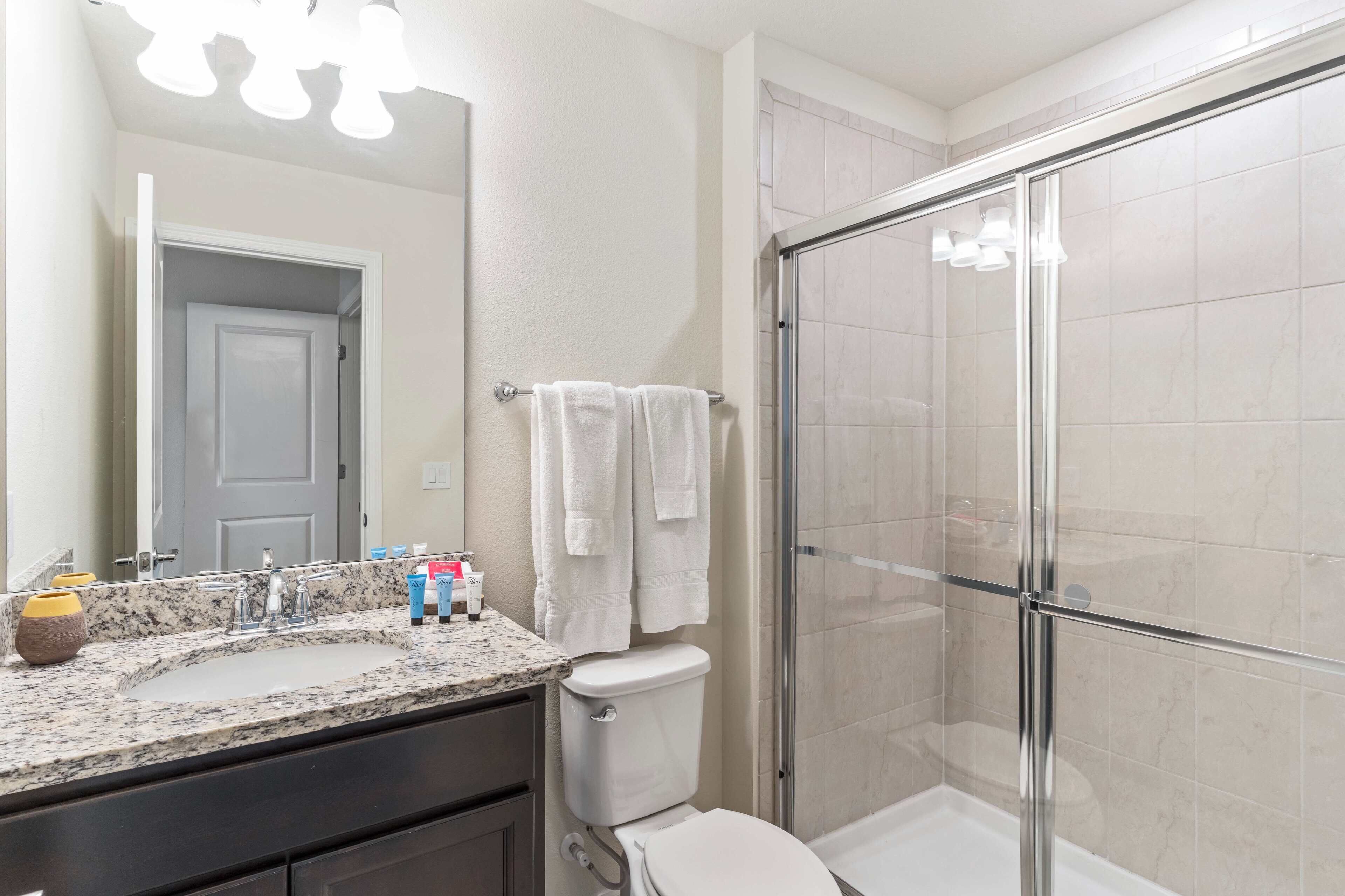 A bathroom with a granite countertop, a toilet, a glass shower enclosure, and a mirror.