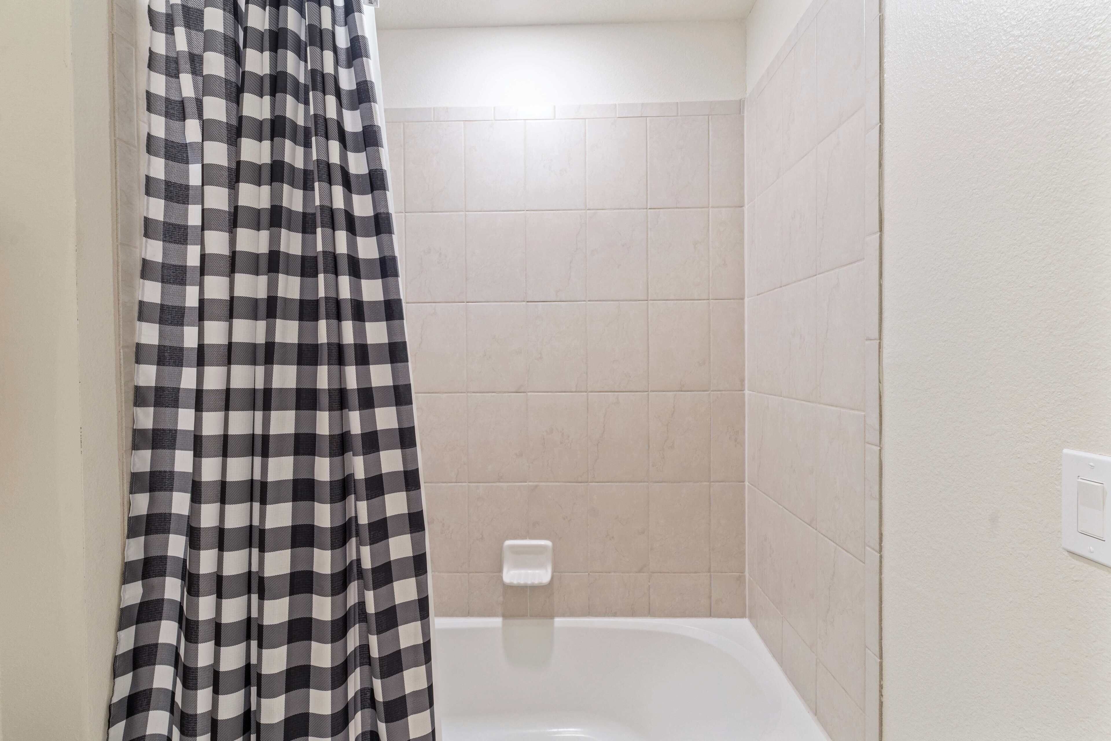 A bathroom with a checkered shower curtain, a white bathtub, and beige tiled walls.