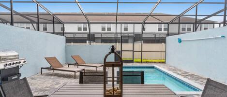 An outdoor patio with a pool, lounge chairs, a grill, and a table.