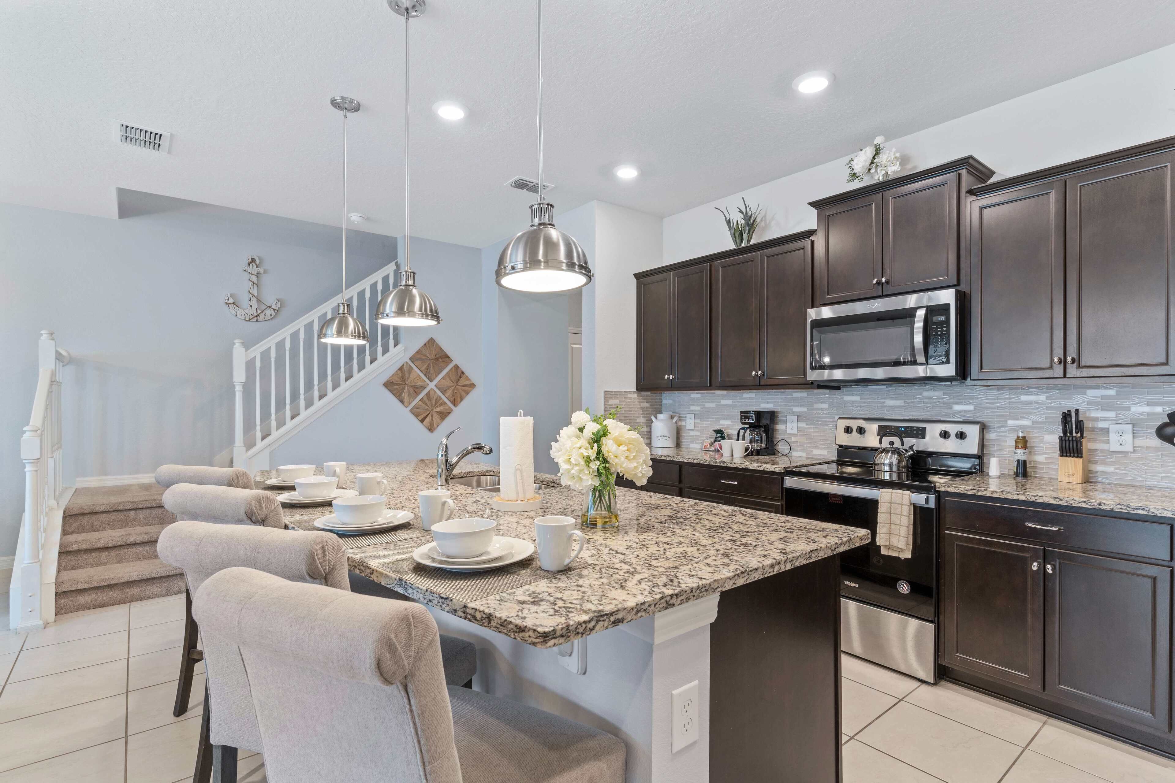 A modern kitchen with dark cabinets, granite countertops, stainless steel appliances, and a central island with seating.