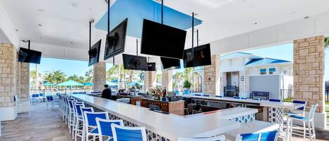 An outdoor bar area with multiple seating arrangements, a long counter, and several flat-screen TVs mounted on the ceiling.