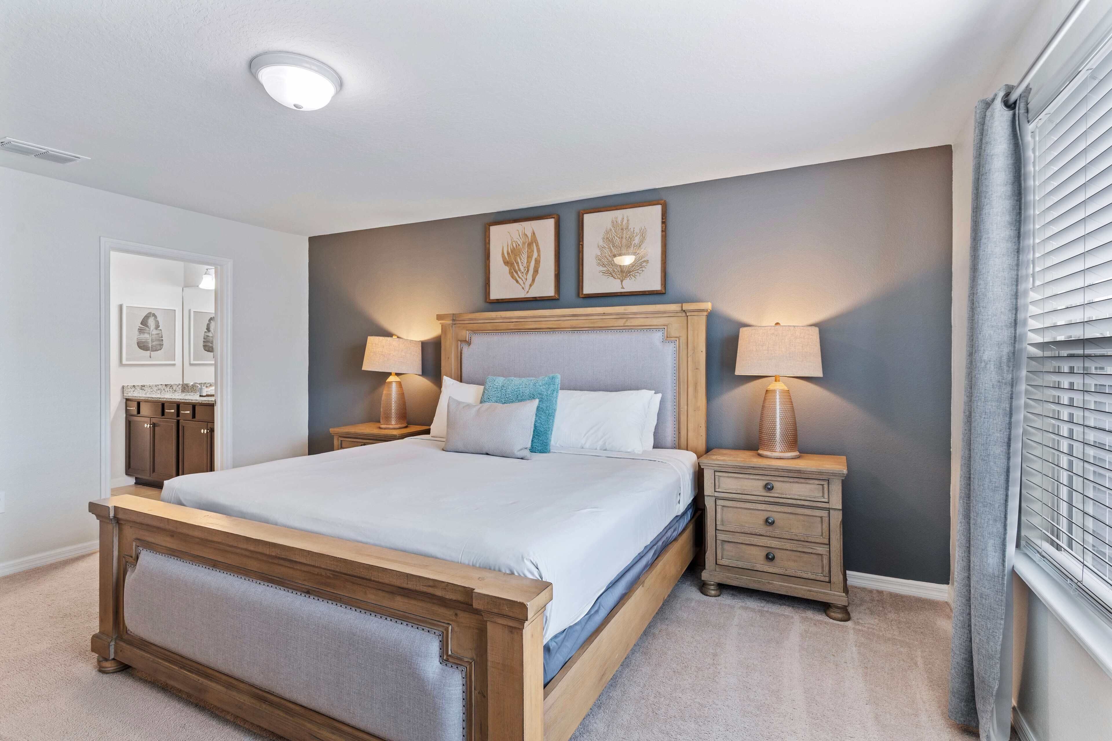 Une chambre à coucher avec un grand lit, deux tables de chevet avec des lampes, une tête de lit et des œuvres d’art encadrées accrochées au mur.
