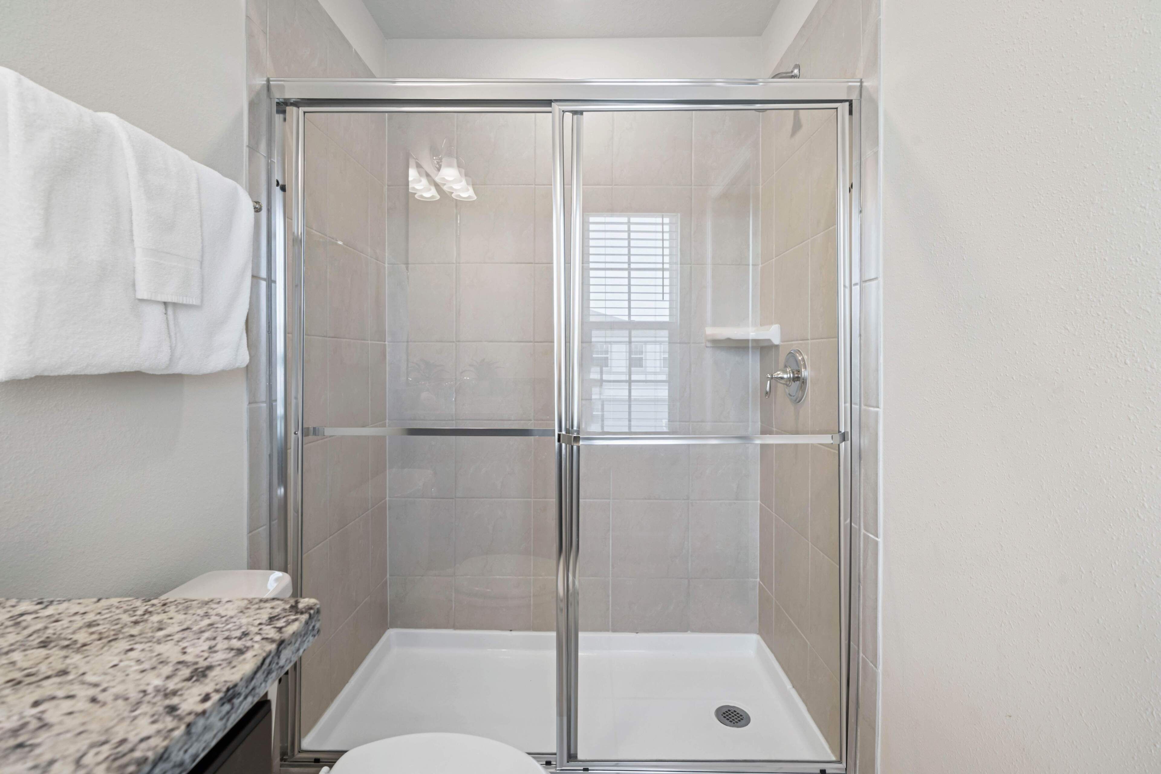 Eine Dusche mit Glastür, eine weiße Toilette und eine Arbeitsplatte aus Granit.