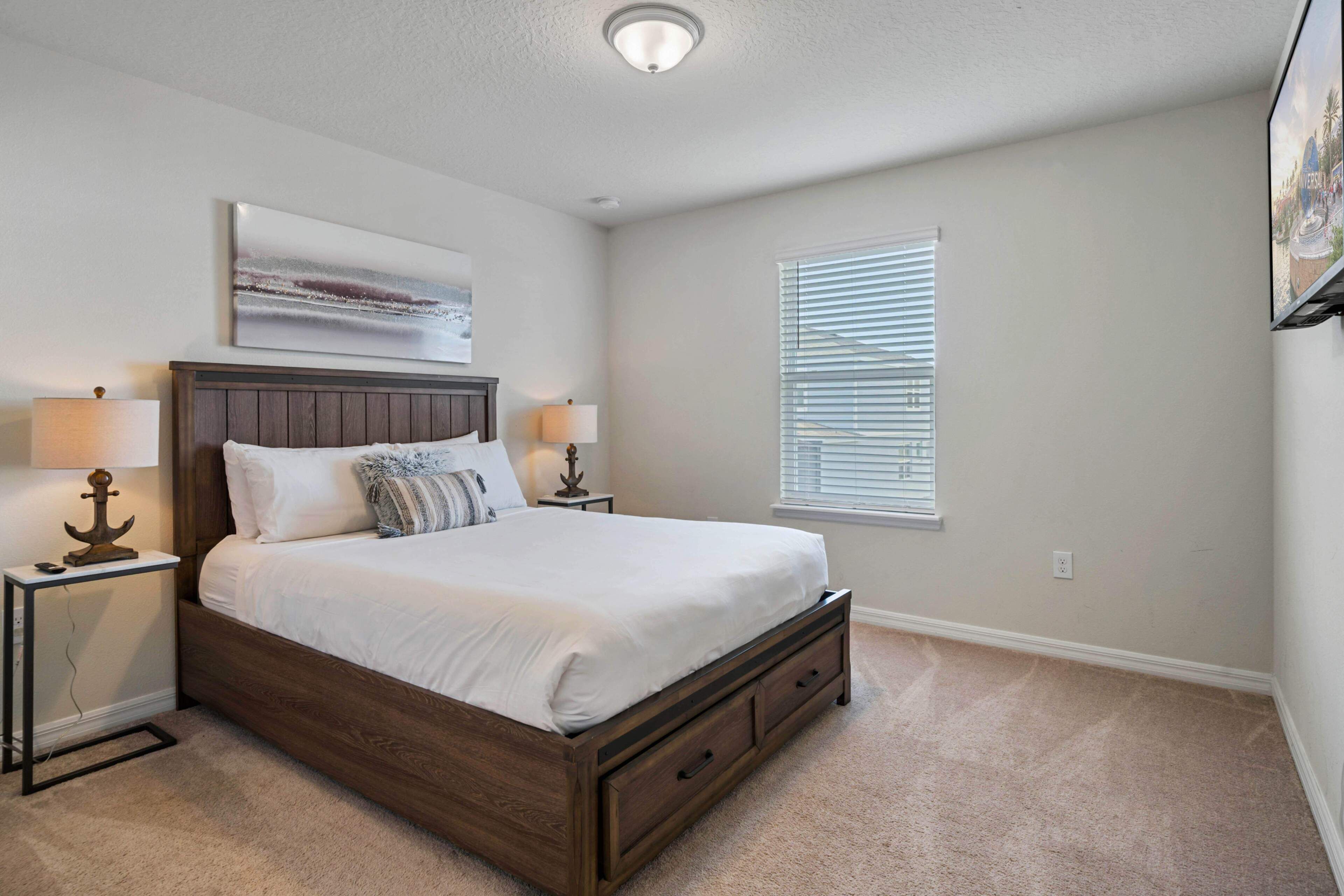 A bedroom with a wooden bed, two bedside tables with lamps, a window with blinds, and a painting on the wall.