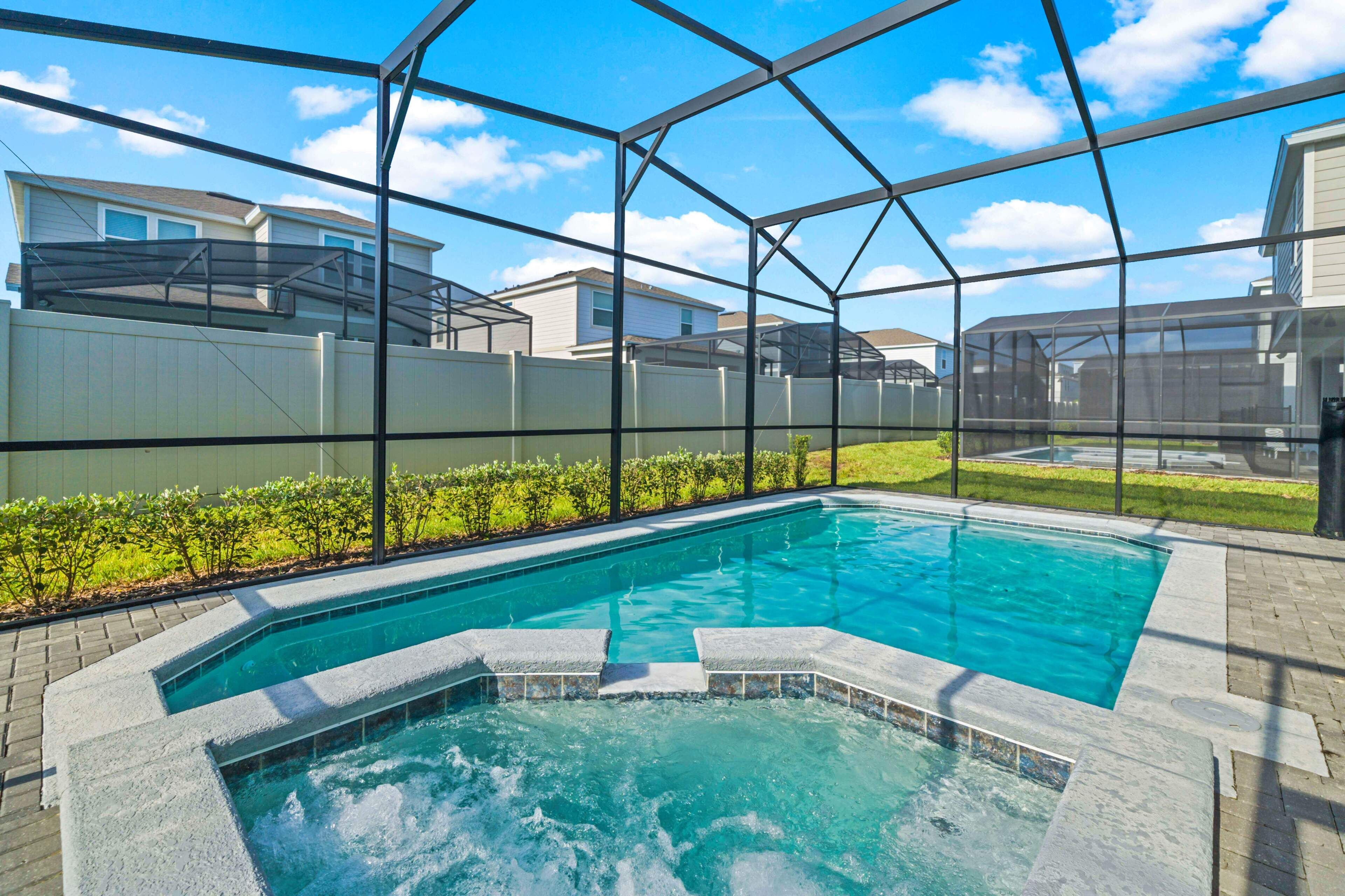 A swimming pool with a hot tub, surrounded by a covered area with a view of neighboring houses.