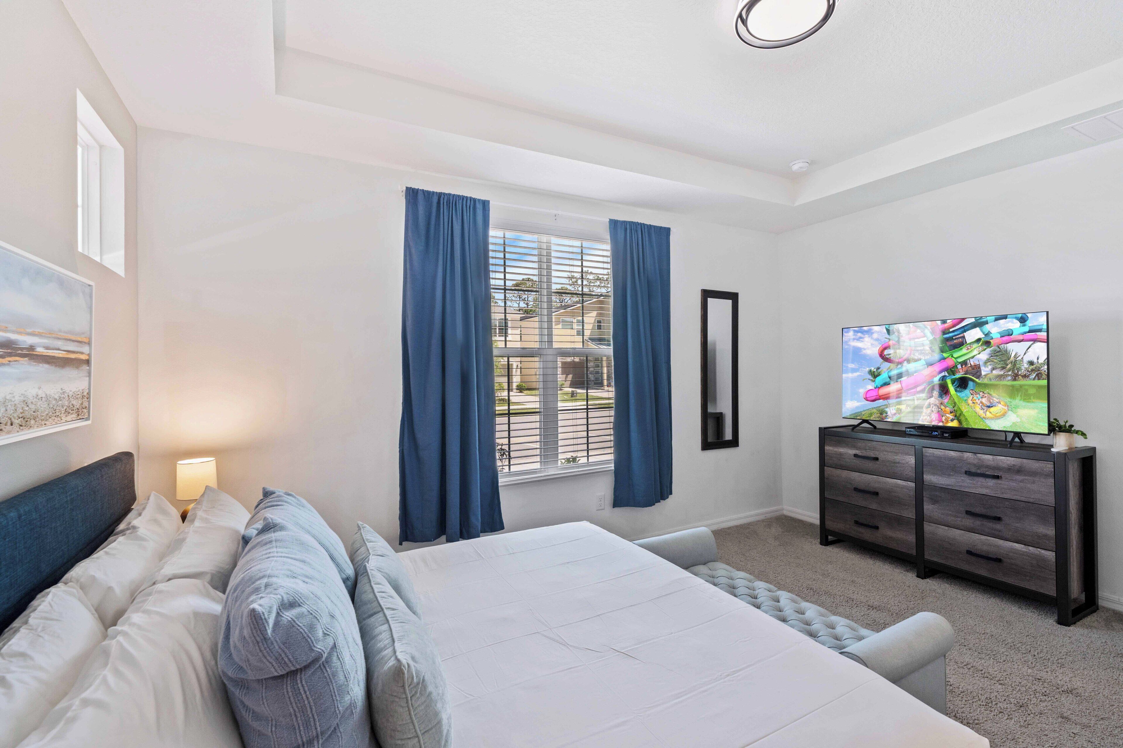 A bedroom with a bed, a TV, a dresser, and a window with curtains.