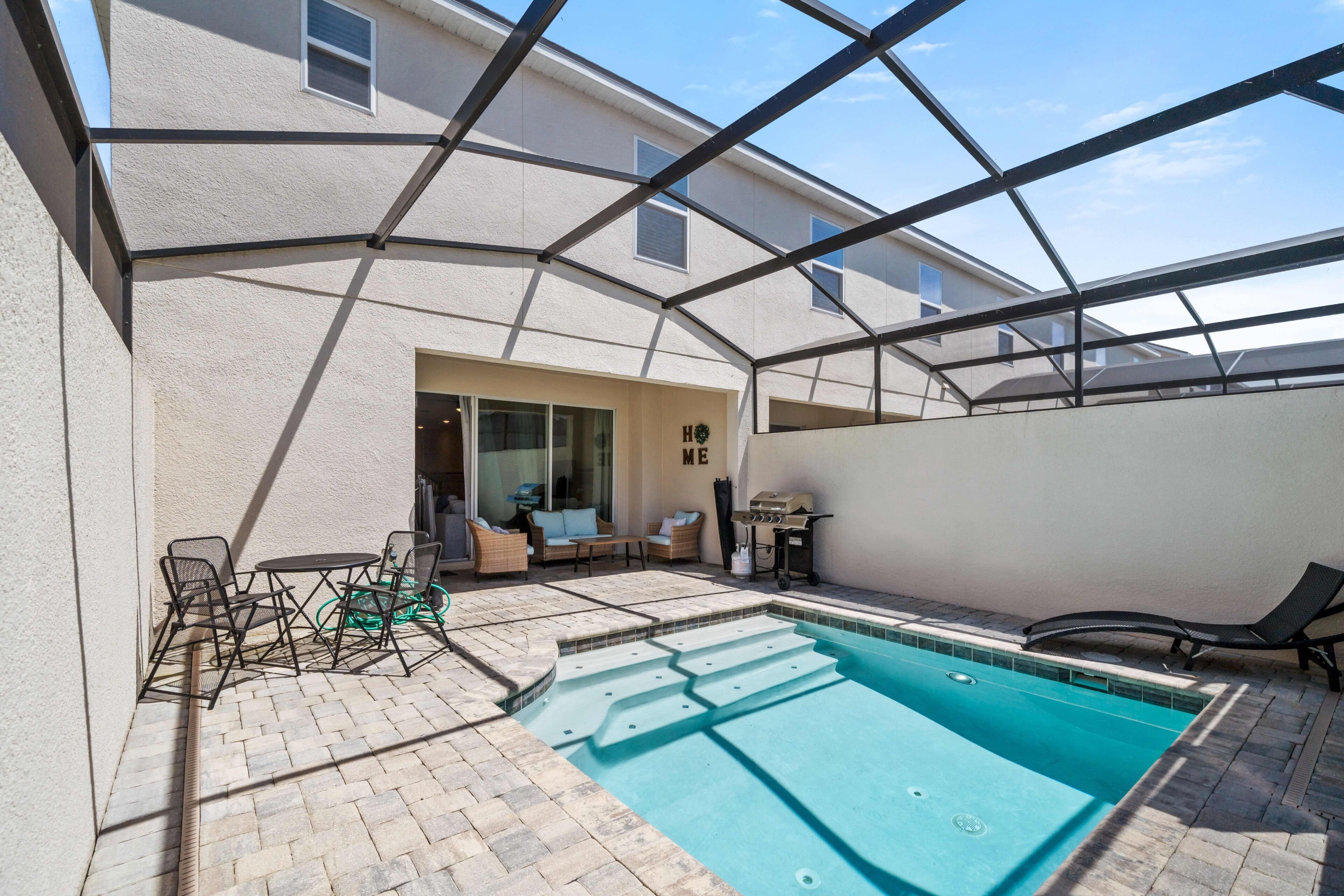 A covered outdoor swimming pool with a patio area, including seating and a grill.