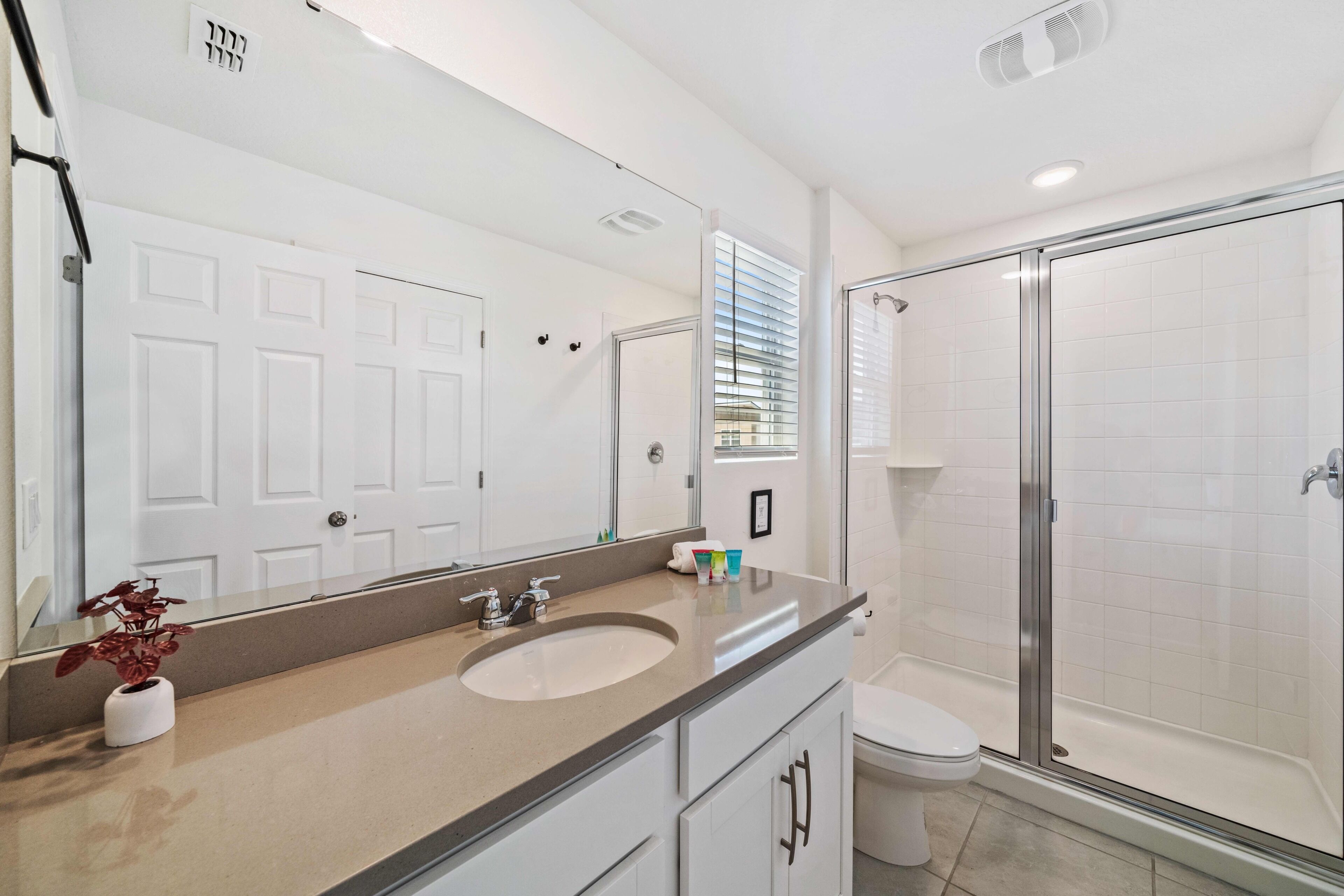 A modern bathroom with a large mirror, a sink, a toilet, and a glass-enclosed shower.