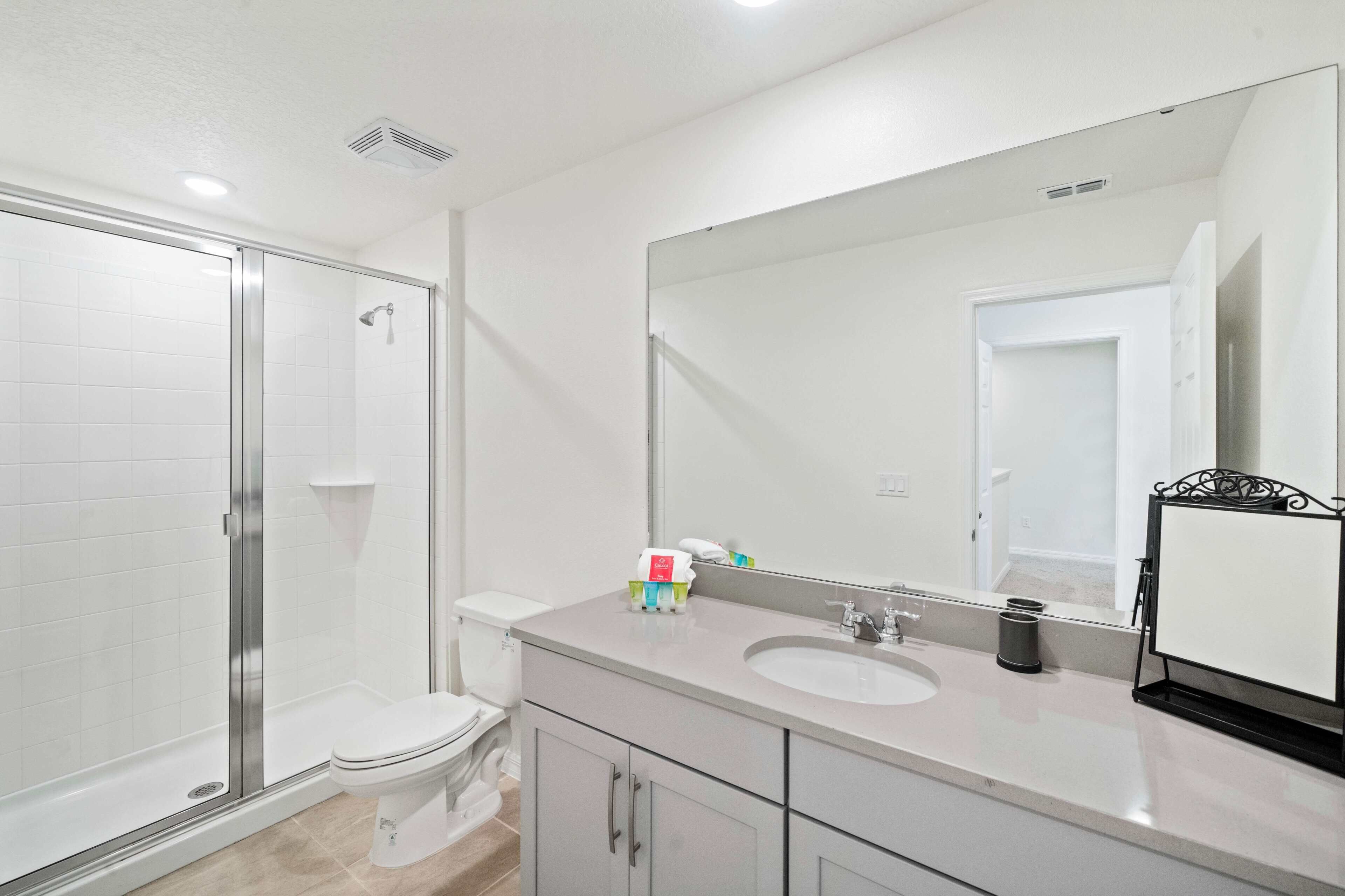 A bathroom with a glass-enclosed shower, a toilet, a sink with a large mirror, and a cabinet.