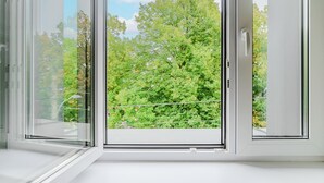 Una habitación con un gran ventanal corredero que da a un balcón con vistas a árboles verdes y un cielo despejado.