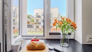 Una encimera de cocina con una hogaza de pan, un cuchillo, un florero con flores y una ventana con vistas a edificios.