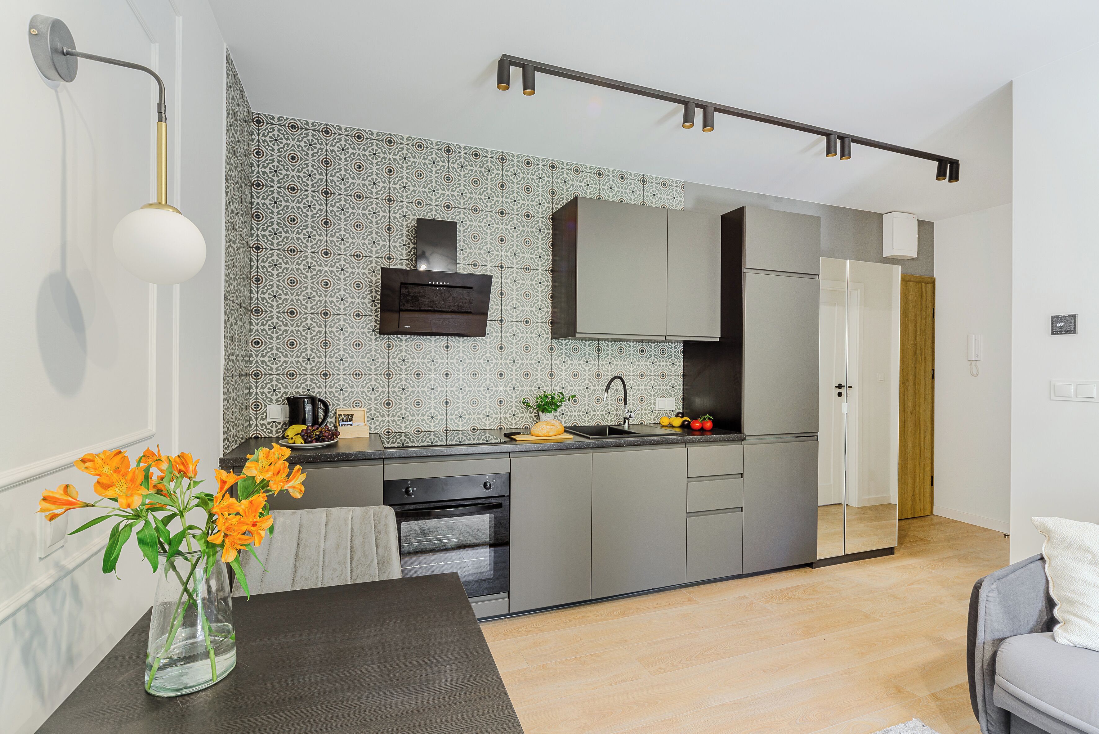 A modern kitchen with grey cabinets, a built-in oven, and a backsplash with a geometric pattern.