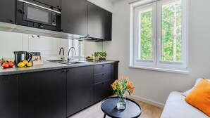Una cocina moderna con armarios oscuros, un microondas y un lavabo. Hay una pequeña mesa con un jarrón de flores y una ventana con vistas a la vegetación.