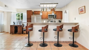 A kitchen with wooden cabinets, a stainless steel refrigerator, a microwave, and three bar stools. - Welcome to Casa de Ladrillos - No House guests without prior approval from host. (Albuquerque)