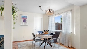 A dining area with a round table, chairs, a chandelier, and a window with curtains. - Welcome to Casa de Ladrillos - No House guests without prior approval from host. (Albuquerque)