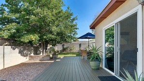 A wooden deck with a view of a backyard, a sliding glass door, and a potted plant. - Welcome to Casa de Ladrillos - No House guests without prior approval from host. (Albuquerque)