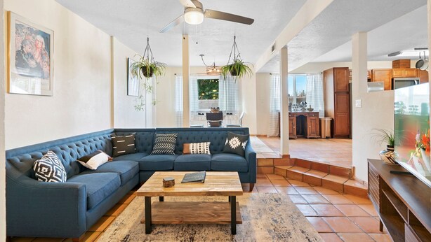 A living room with a sectional sofa, a coffee table, hanging plants, and a ceiling fan. - Welcome to Casa de Ladrillos - No House guests without prior approval from host. (Albuquerque)